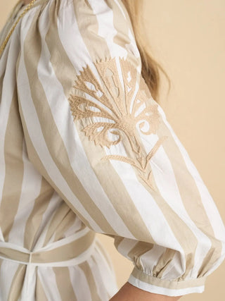Close-up of a beige and white striped garment with intricate embroidery on a beige background