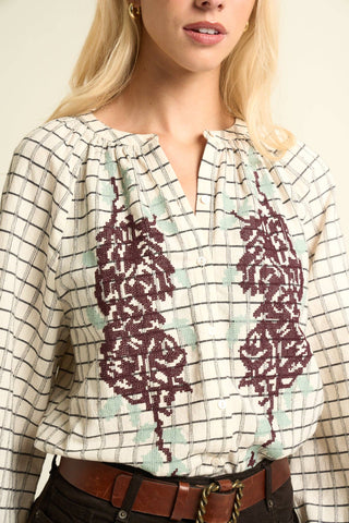 Woman wearing a patterned blouse with a plaid design and floral accents.