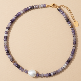 Necklace with purple and white beads and a gold chain on a beige background