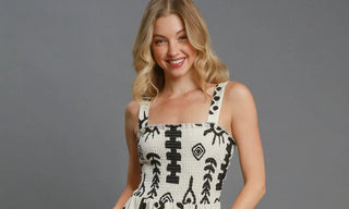 Woman wearing a cream jumpsuit with black geometric patterns on a gray background