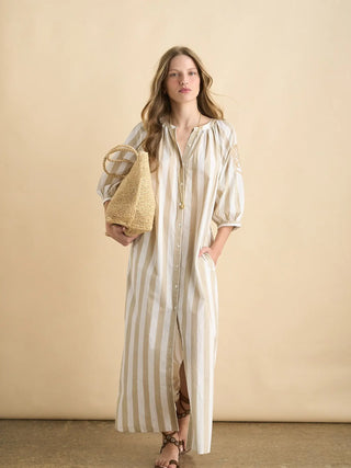 Woman wearing a long striped dress holding a woven bag against a beige background