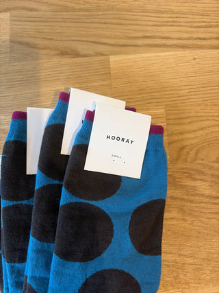 Blue socks with black dots and 'HOORAY' tags on a wooden surface