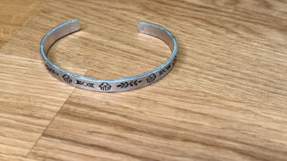 Silver bracelet with engraved designs on a wooden surface