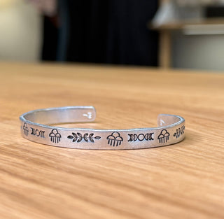 Silver bracelet with rain clouds, leaves and waxing/waning mooms engraved designs, sitting on a wooden surface