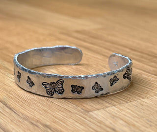 Silver bracelet with butterfly designs on a wooden surface