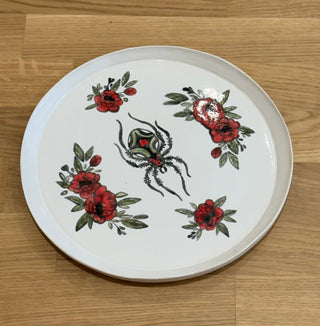 Round ceramic plate with floral and spider design on a wooden floor