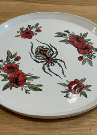 Decorative plate with spider and floral design on a wooden surface