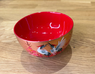 Red ceramic bowl with bird design on a wooden surface