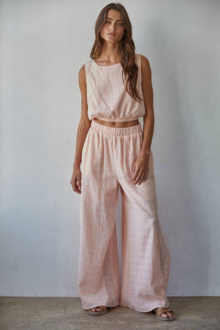 Woman wearing a light pink sleeveless top and wide-leg pants against a plain background