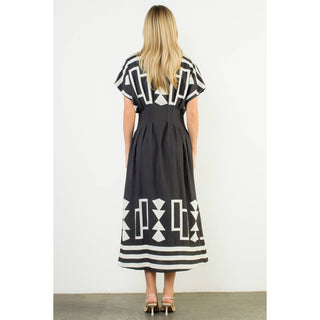 Woman wearing a black dress with white geometric patterns on a plain background