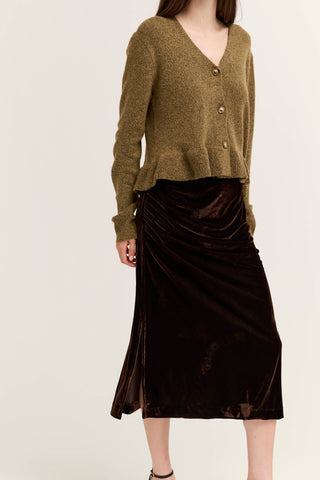 A model wearing a cropped olive green knit cardigan and a dark brown velvet midi skirt, shown from the neck down against a plain off-white background.