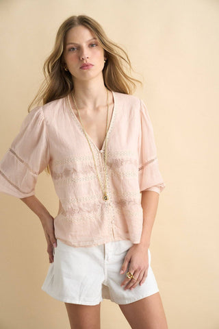 Woman wearing a light pink blouse with a zipper and white shorts on a beige background