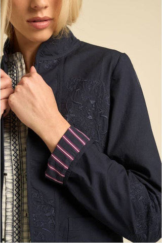 Close-up of a model wearing a dark navy embroidered jacket with a high stand collar and a striped cuff, paired with a patterned shirt.