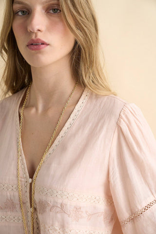 Woman wearing a light pink lace-trimmed top with a neutral background